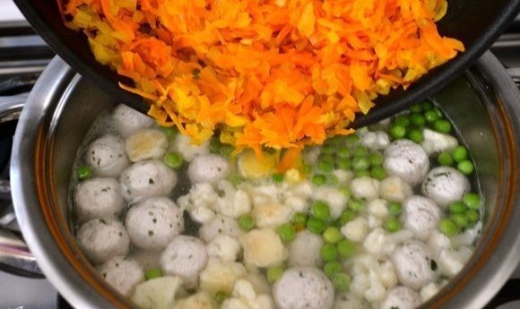 овощная зажарка опускается в кастрюлю с супом из зеленого горошка и соцветий цветной капусты