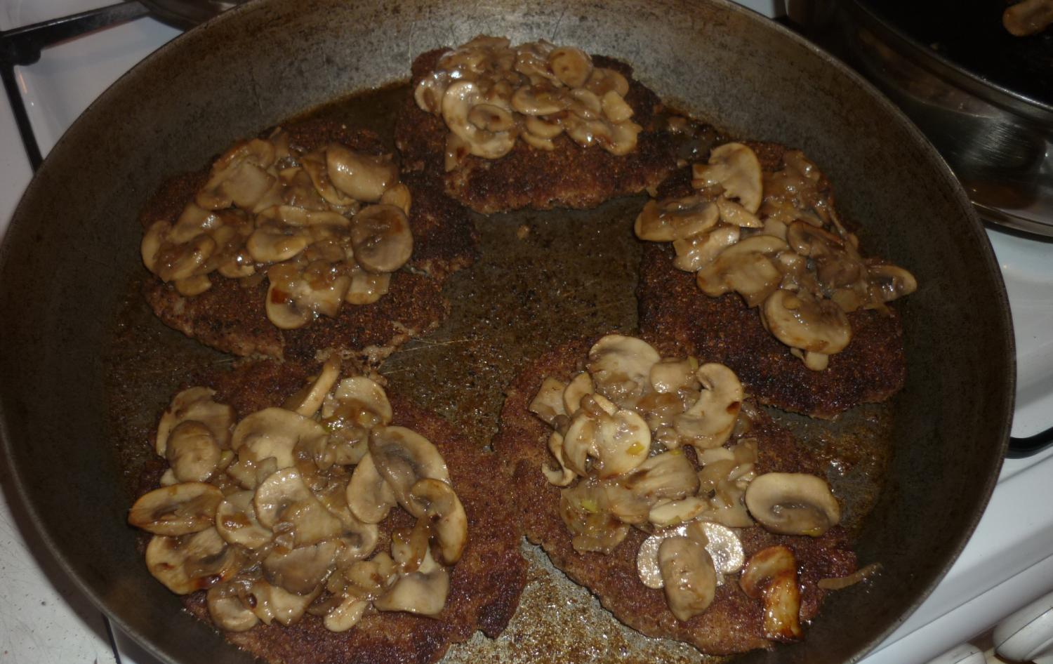 котлеты в сковороде, сверху на них лежат обжаренные грибы